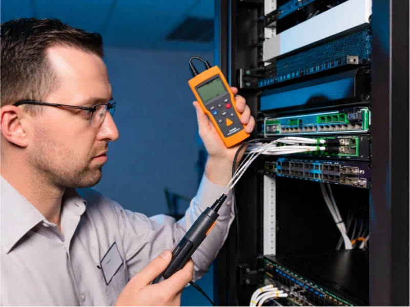 Data center technician working on server rack, tracing fiber optic cables with VFL and power meter to troubleshoot MPO polarity errors, insertion loss, and network link failures.